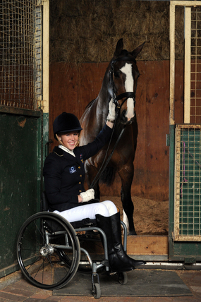 Photo of Grace Bowman dressed in riding gear, seated in her wheelchair and with her horse