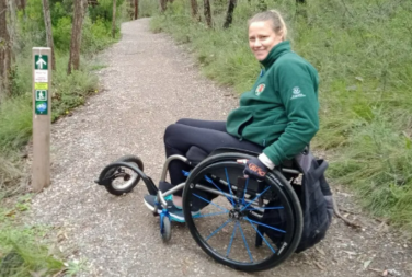 Photo of Yvie Eglinton in her wheelchair, on a trail in a park