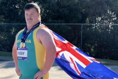 Photo of Hugo Teheny wearing his medals round his neck, and with the Australian flag behind him
